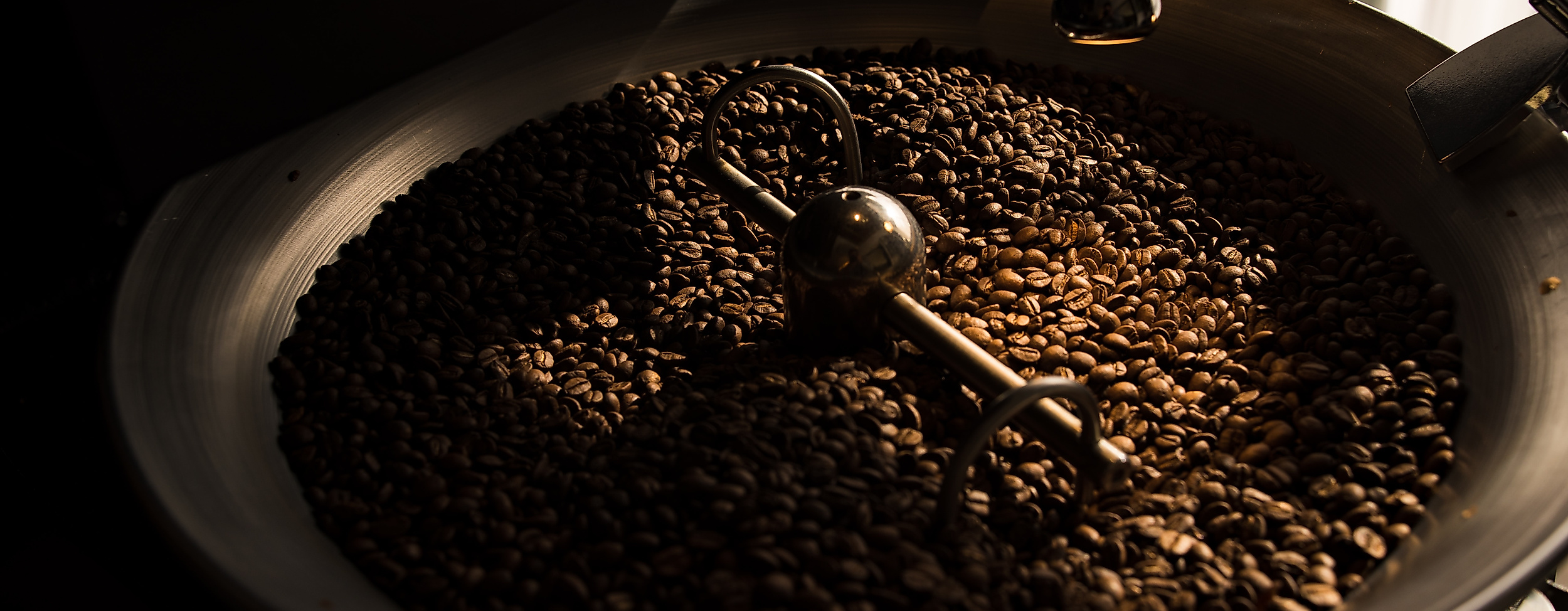 Frisch geröstete Kaffeebohnen in einer Rösttrommel, beleuchtet durch warmes Licht.