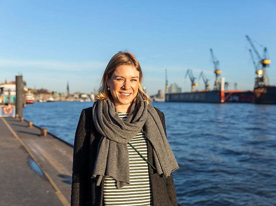 Frau am Hamburger Hafen bei Sonnenschein mit Blick auf die Elbe und Werftkräne im Hintergrund