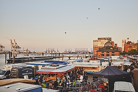 Marktbetrieb am Hamburger Fischmarkt mit vielen Ständen, Menschen und Blick auf Hafenkräne