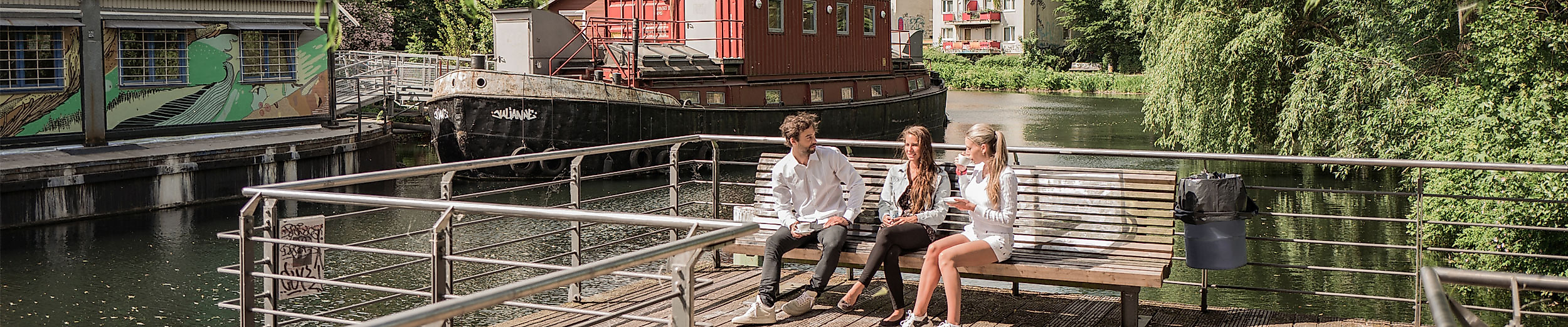 Menschen entspannen an einem Holzsteg am Wasser im alternativen Kultur- und Gartenprojekt Zomia in Wilhelmsburg.