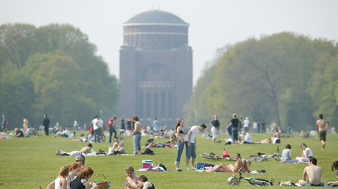 Menschen entspannen auf der großen Wiese im Hamburger Stadtpark mit Blick auf das Planetarium bei Frühlingstemperaturen
