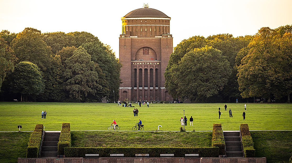 Grüne Wiese mit Besucher:innen vor dem Hamburger Planetarium im Stadtpark bei warmem Abendlicht