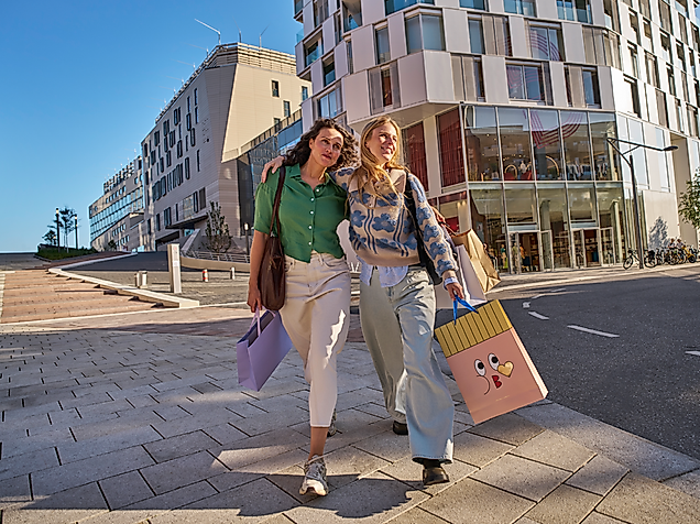 Zwei Frauen schlendern bei Sonnenschein an der Hamburger Alster vor dem Westfield