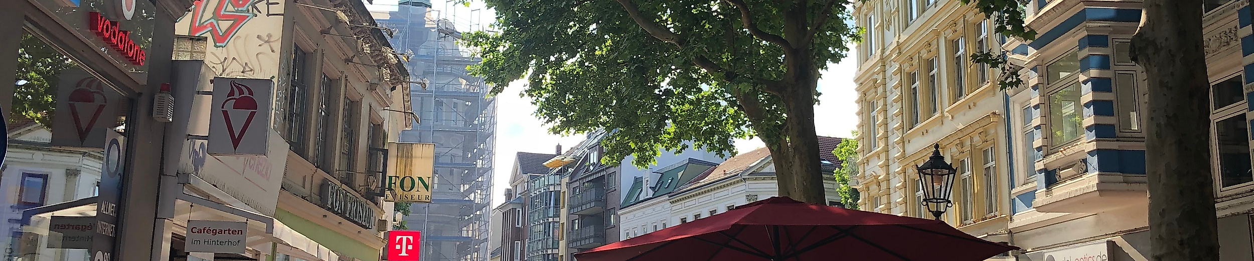 Belebte Ottensener Hauptstraße in Hamburg mit Geschäften, Straßencafés und Passant:innen im Sonnenlicht