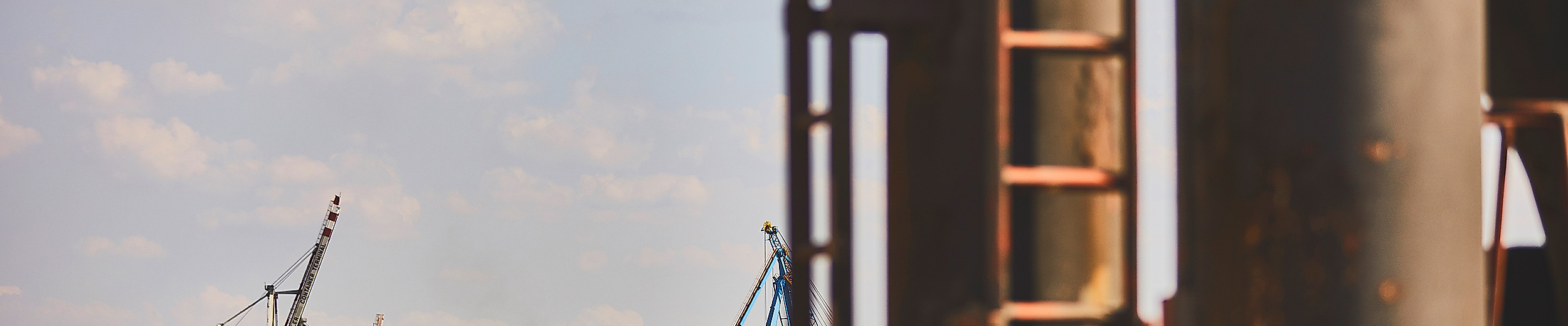 Industrielle Hafenansicht in Hamburg mit rostiger Leiter im Vordergrund und Kränen im Hintergrund