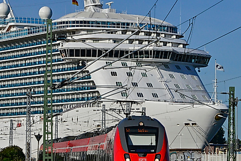 Regionalzug auf Gleisen im Hintergrund großes Kreuzfahrtschiff