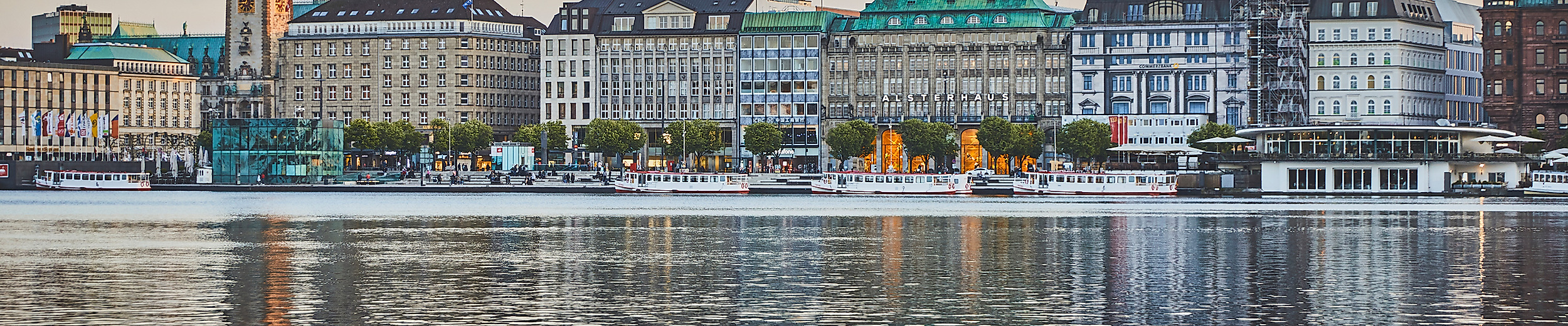 Binnenalster im Hintergrund Jungfernstieg und Hamburger Altstadt mit Rathaus und Kirchturm bei Abenddämmerung.