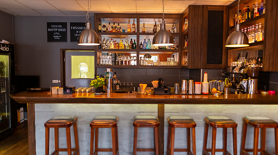 Stilvolle Bar des Restaurant Flutliche mit Holztheke, Hockern und beleuchtetem Regal mit Spirituosen in gemütlicher Atmosphäre