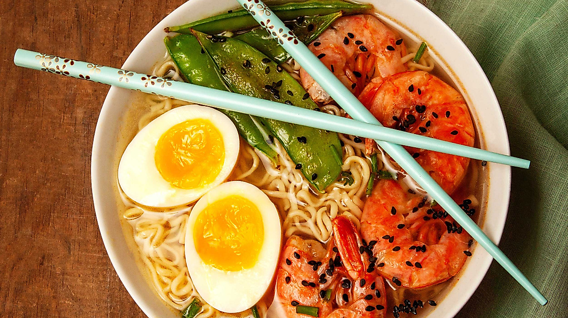Schüssel Ramen mit Ei, Garnelen, Gemüse und Nudeln, dekorativ angerichtet mit Essstäbchen