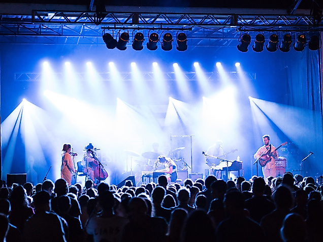 Publikum vor hell beleuchteter Bühne bei Live-Konzert mit Band und Scheinwerfern