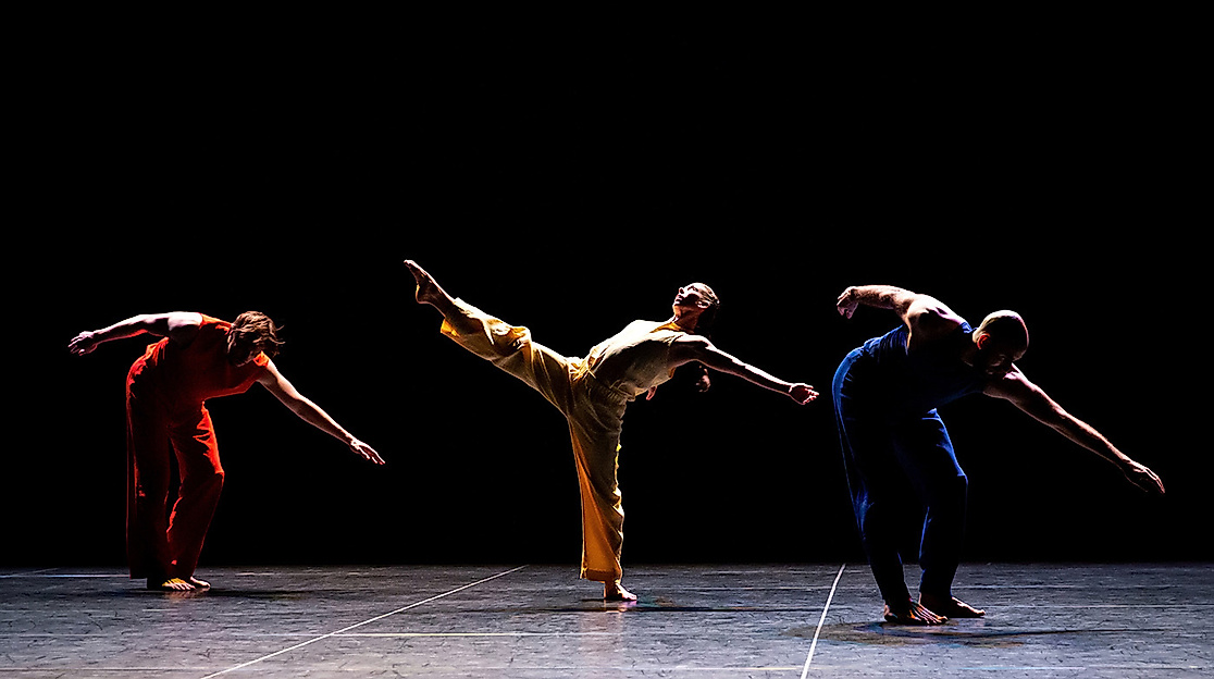 Die Performer*innen Patrick Needham, Cecily Campbell und Burr Johnson tanzen auf der Bühne, ihre Arme und Beine sind energievoll und ausdrucksstark nach außen gestreckt.