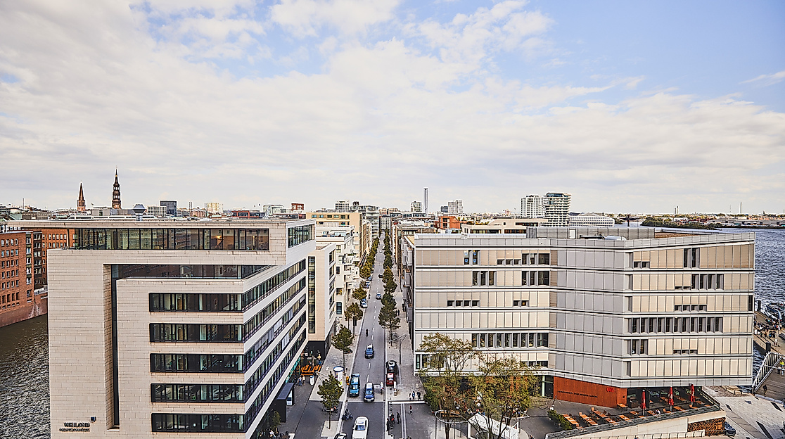 Überseeboulevard in der HafenCity Hamburg mit moderner Bebauung, Cafés und Passant:innen bei Tageslicht