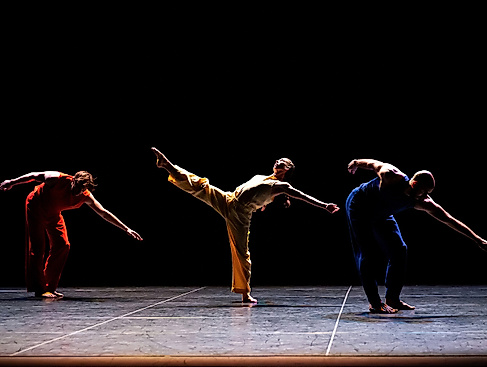 Die Performer*innen Patrick Needham, Cecily Campbell und Burr Johnson tanzen auf der Bühne, ihre Arme und Beine sind energievoll und ausdrucksstark nach außen gestreckt.