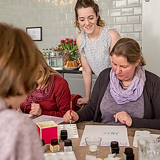 Workshop-Leiterin unterstützt Teilnehmende beim kreativen Lettering an einem Tisch mit Übungsblättern und Tinte