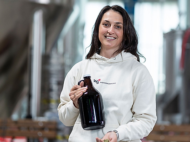Frau in heller Kleidung hält dunkle Bierflasche in Brauerei bei der Hamburg Beer Week.