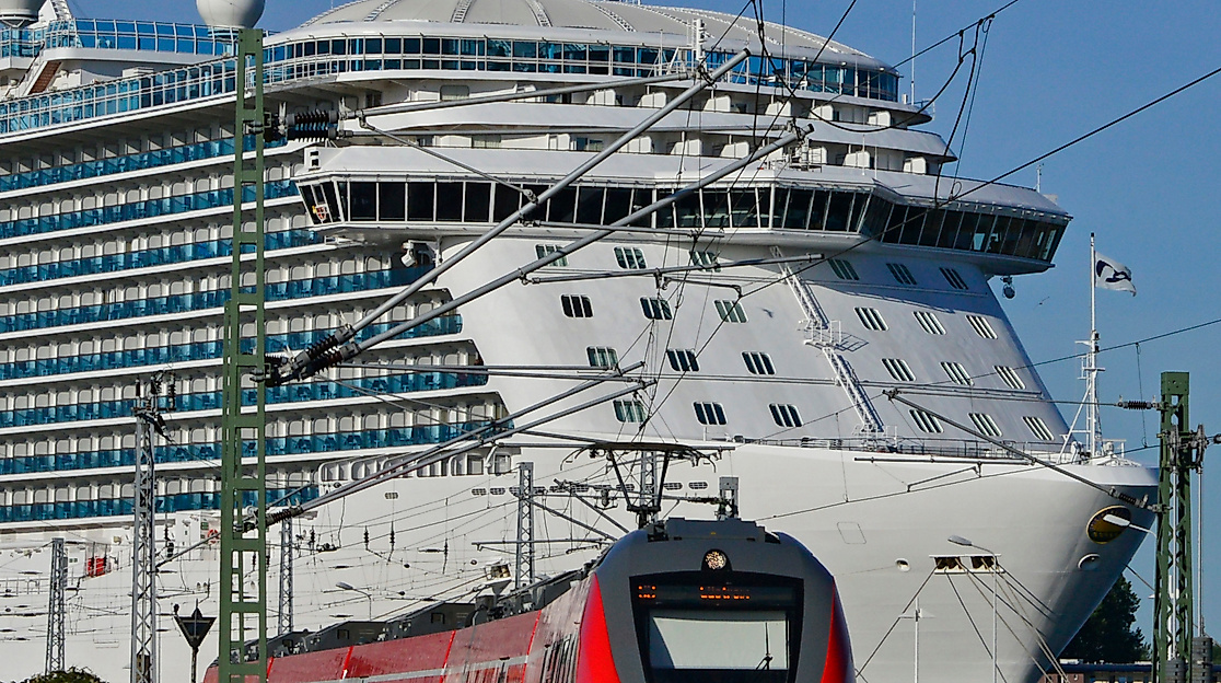 Regionalzug auf Gleisen im Hintergrund großes Kreuzfahrtschiff