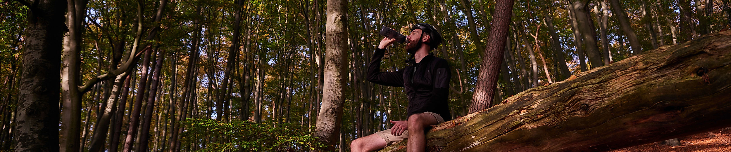 Radfahrer pausiert auf Baumstamm im herbstlichen Wald und genießt die Natur bei Sonnenlicht