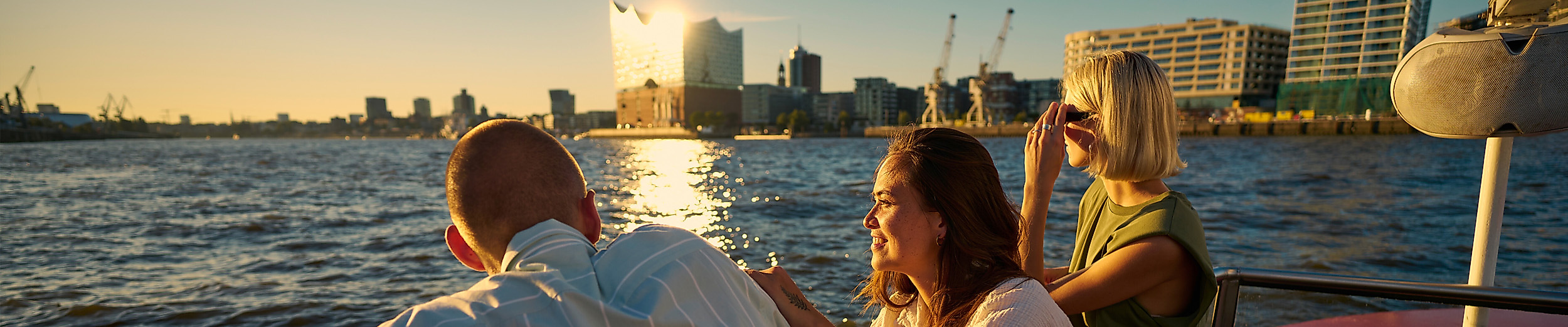 Junge Erwachsene auf einem Boot auf der Elbe. Im Hintergrund ist die Elphi zu sehen.