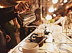 Barista gießt frischen Kaffee in Tassen an beleuchteter Theke mit gemütlicher Atmosphäre