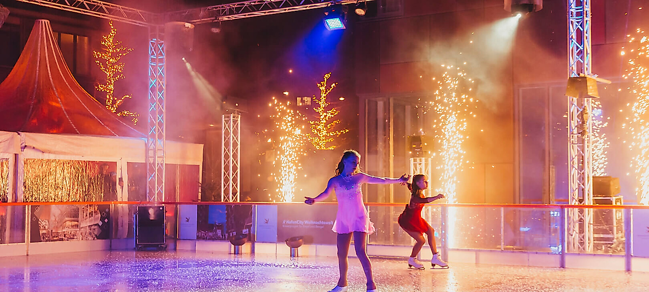 Eisläufer:innen auf festlich beleuchteter Eisbahn mit Lichterglanz und winterlicher Stimmung in Hamburg. Begründung:
