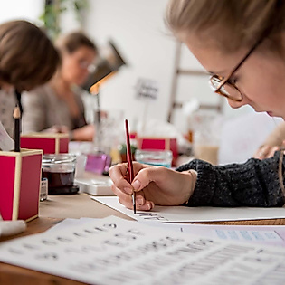 Teilnehmende üben konzentriert verschiedene Lettering-Stile mit Pinsel und Vorlage beim kreativen Workshop