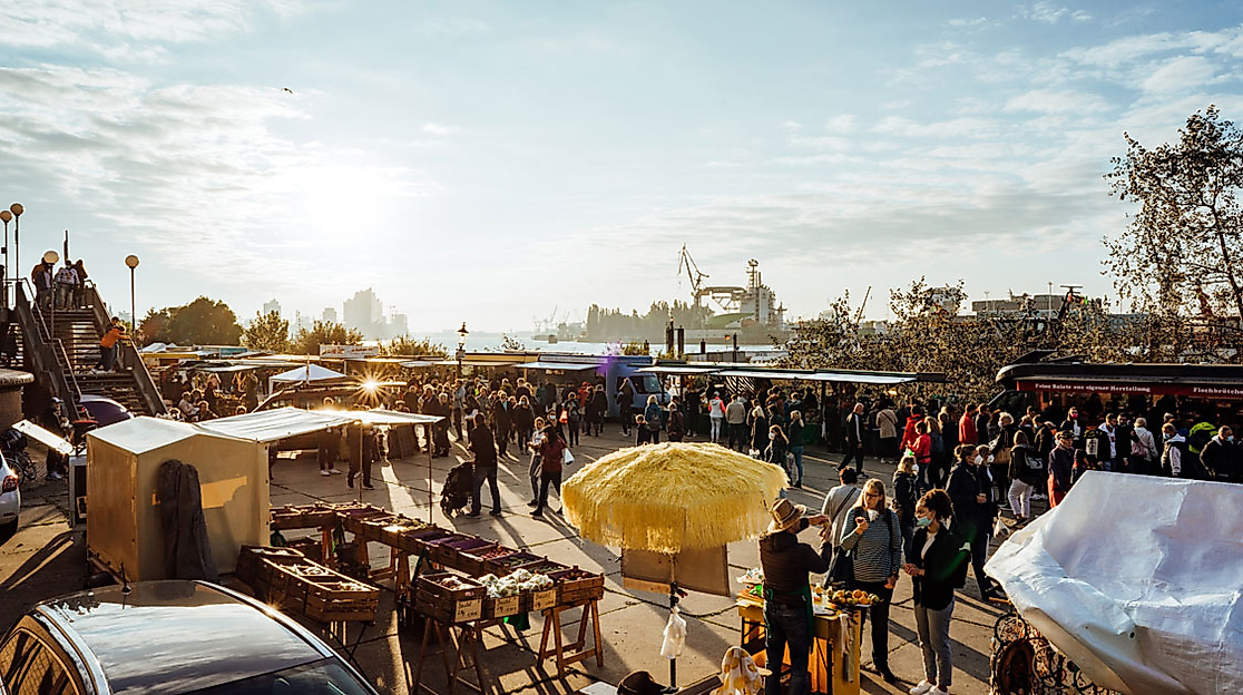 Vormittagsstimmung auf dem Fischmarkt in Hamburg mit zahlreichen Marktständen, Besucher:innen und Blick auf den Hafen