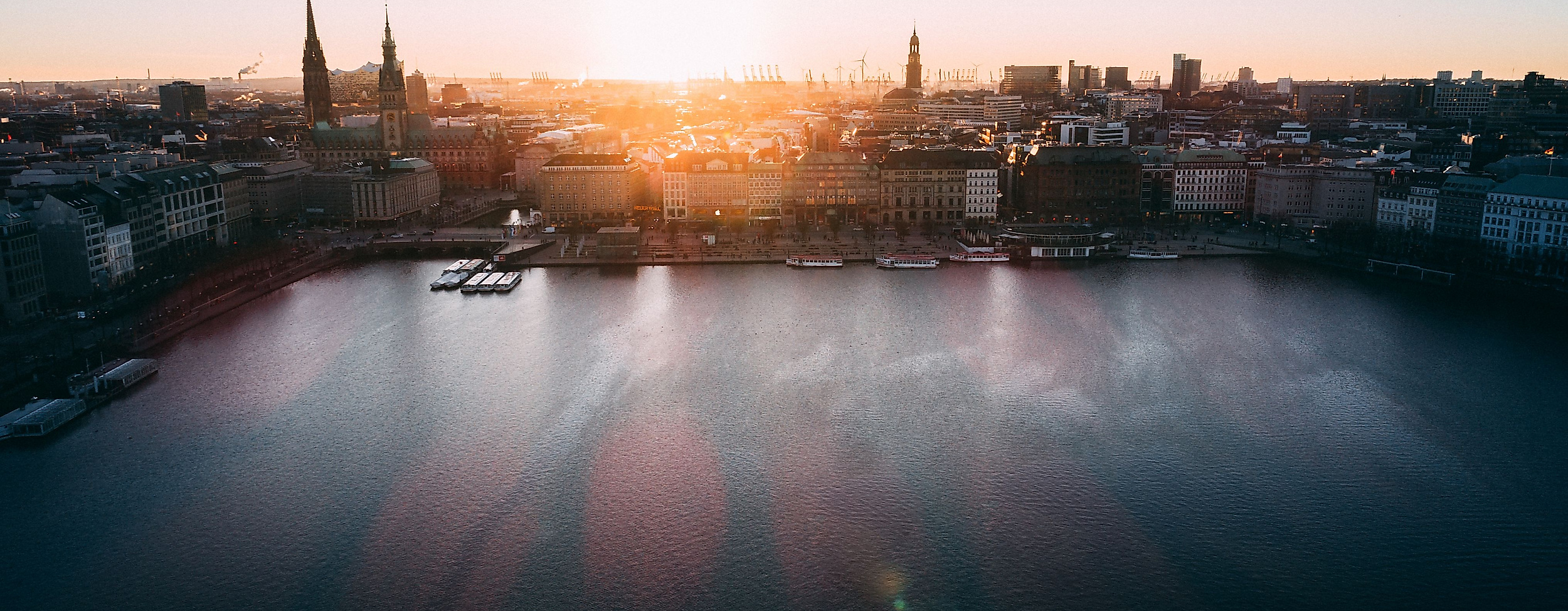 Panoramablick auf die Binnenalster bei Sonnenuntergang mit Kirchtürmen der Hamburger Altstadt.