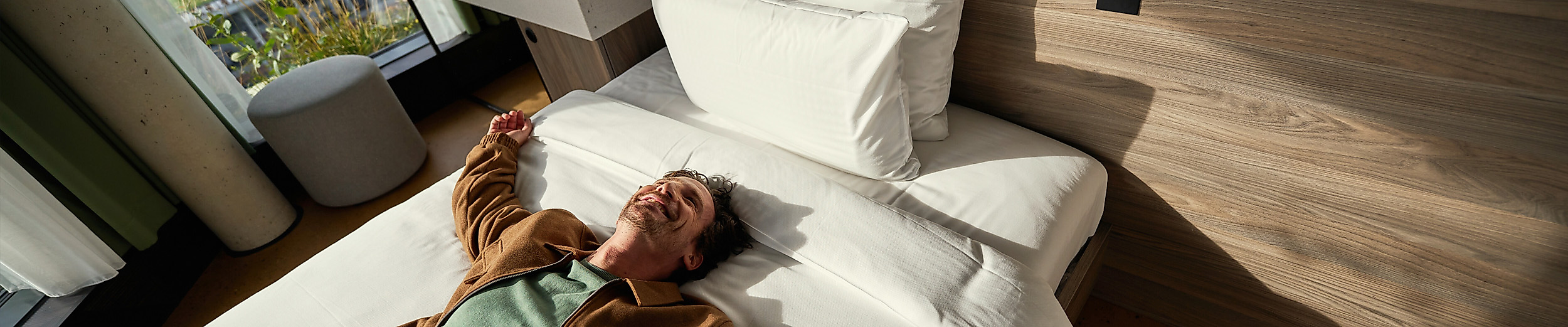 Ein Mann liegt mit ausgestreckten Armen auf dem Bett eines Hotelzimmers.