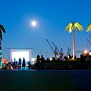 Beleuchtete Palmen und Open-Air-Kino bei Nacht im Park Fiction mit Blick auf Hafen und Vollmond