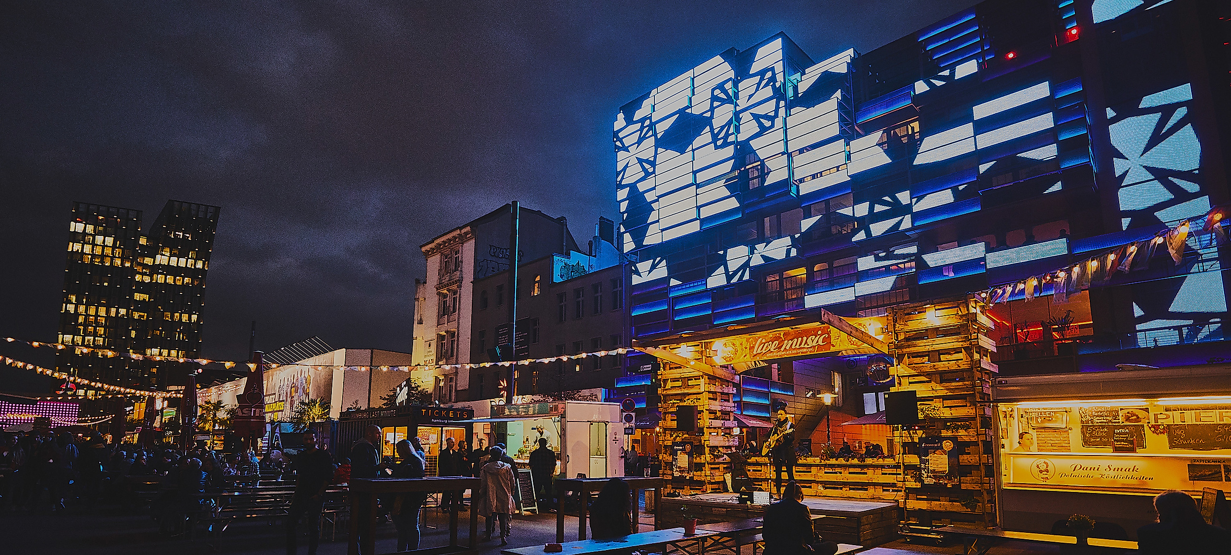 Beleuchtete Fassaden und Street-Food-Stände auf dem Spielbudenplatz in Hamburg-St. Pauli bei Nacht