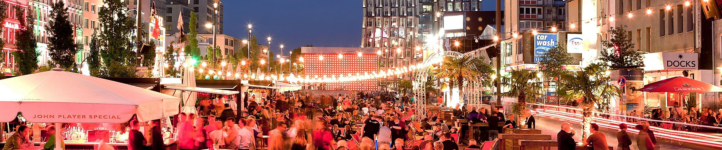 Belebte Abendstimmung auf der Reeperbahn in Hamburg mit Lichterketten, Straßencafés und tanzenden Türmen im Hintergrund