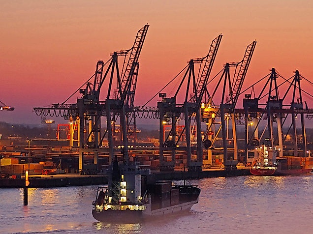 Containerhafen im Hamburger Hafen bei Sonnenuntergang mit Frachtschiff und beleuchteten Kränen