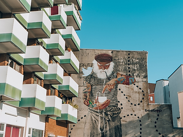 Großes Street-Art-Porträt auf einer Hauswand zwischen modernen Wohngebäuden mit Balkonfassade