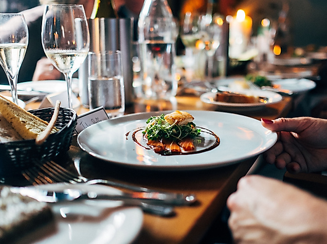 Fein gedeckter Restauranttisch mit Wein und stilvoll angerichtetem Hauptgericht in geselliger Runde