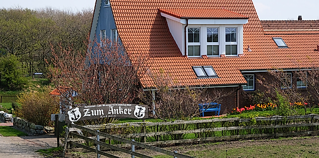 Restaurant Zum Anker auf der Insel Neuwerk mit rotem Ziegeldach, Garten und Beschilderung am Zaun