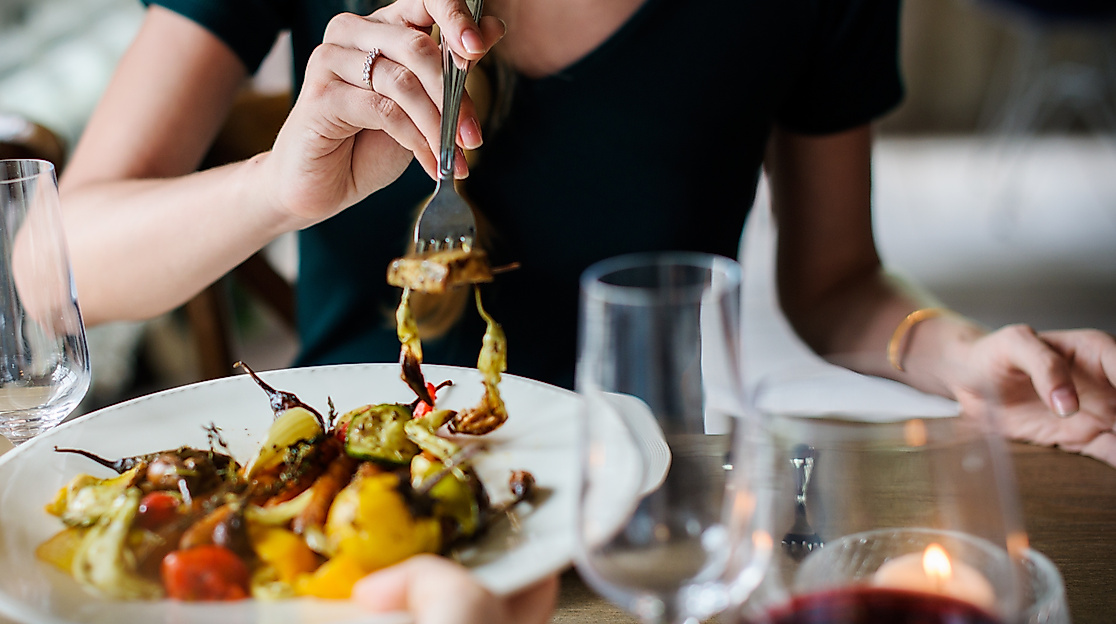 Person isst buntes Gemüsegericht bei Kerzenschein und Wein an stilvoll gedecktem Tisch
