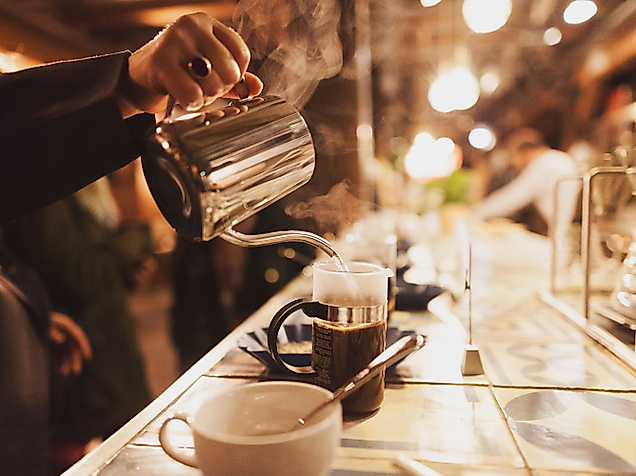 Barista gießt frischen Kaffee in Tassen an beleuchteter Theke mit gemütlicher Atmosphäre
