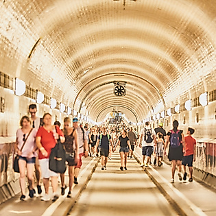 Zahlreiche Fußgänger:innen im hell beleuchteten Tunnelröhrengewölbe des Alten Elbtunnels in Hamburg