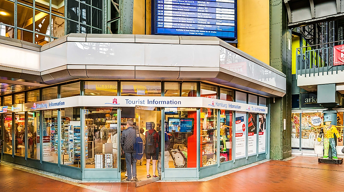 Eingang der Tourist-Information im Hauptbahnhof Hamburg mit großem Infoschild und digitaler Anzeigetafel.