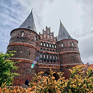 Backstein-Holstentor in Lübeck mit Türmen und Blumen im Vordergrund – Ausflugsziel ab Hamburg an die Ostsee