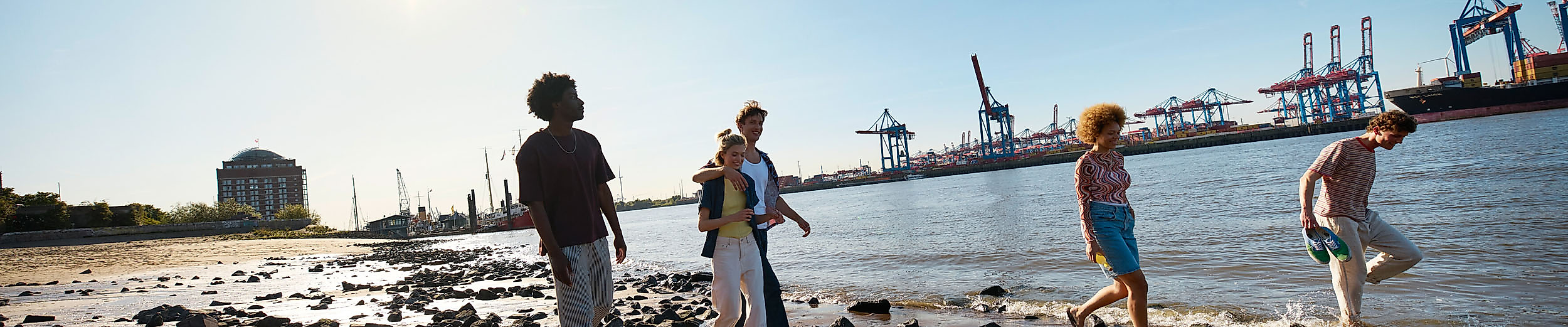 Vier junge Menschen machen unter blauem Himmel einen Spaziergang am Elbstrand.