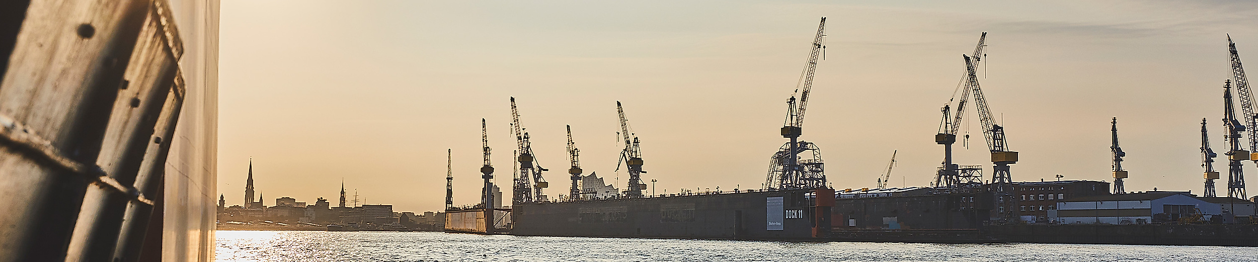 Sonnenaufgang über dem Hamburger Hafen mit spiegelndem Wasser und Hafenkränen im Gegenlicht