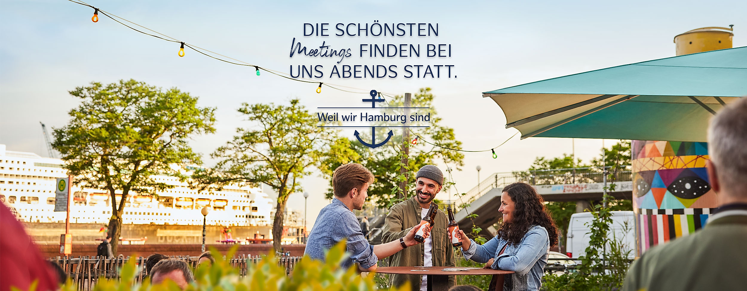 Menschen genießen Bier und Sonne unter Lichterketten auf der Hamburg Beer Week im Freien. Text: "Die schönsten Meetings finden bei uns abends statt". Weil wir Hamburg sind.