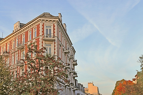 Gründerzeitfassade in Hamburg-Eppendorf im Abendlicht vor herbstlich gefärbten Bäumen und blauem Himmel