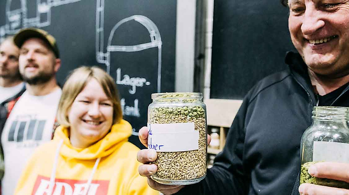 Teilnehmer:innen der Hamburg Beer Week mit Gläsern voller Hopfen vor beschrifteter Tafel