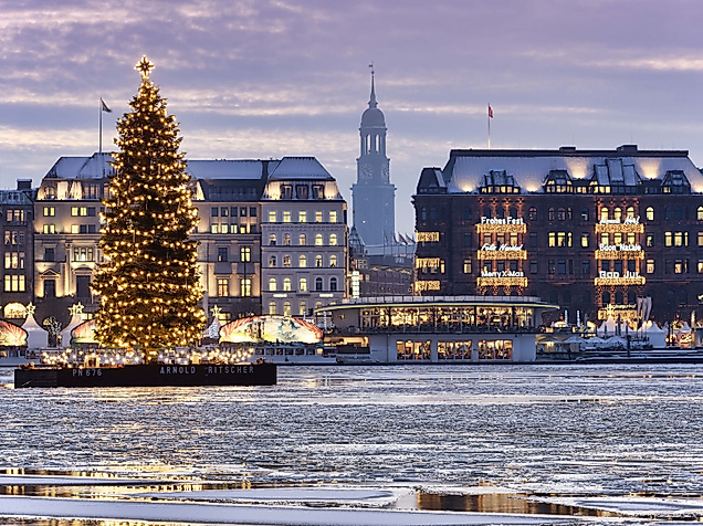 Beleuchteter Weihnachtsbaum auf der winterlichen Binnenalster vor verschneiter Hamburger Kulisse