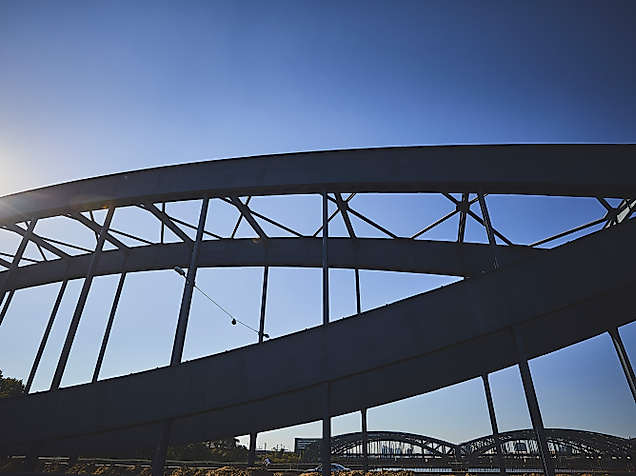 Stählerner Brückenbogen der Elbbrücken vor blauem Himmel im Gegenlicht der Sonne