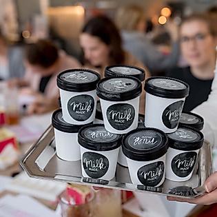 Tablett mit Coffee-to-go-Bechern vor Workshop-Tisch, an dem Teilnehmende kreativ mit Lettering arbeite