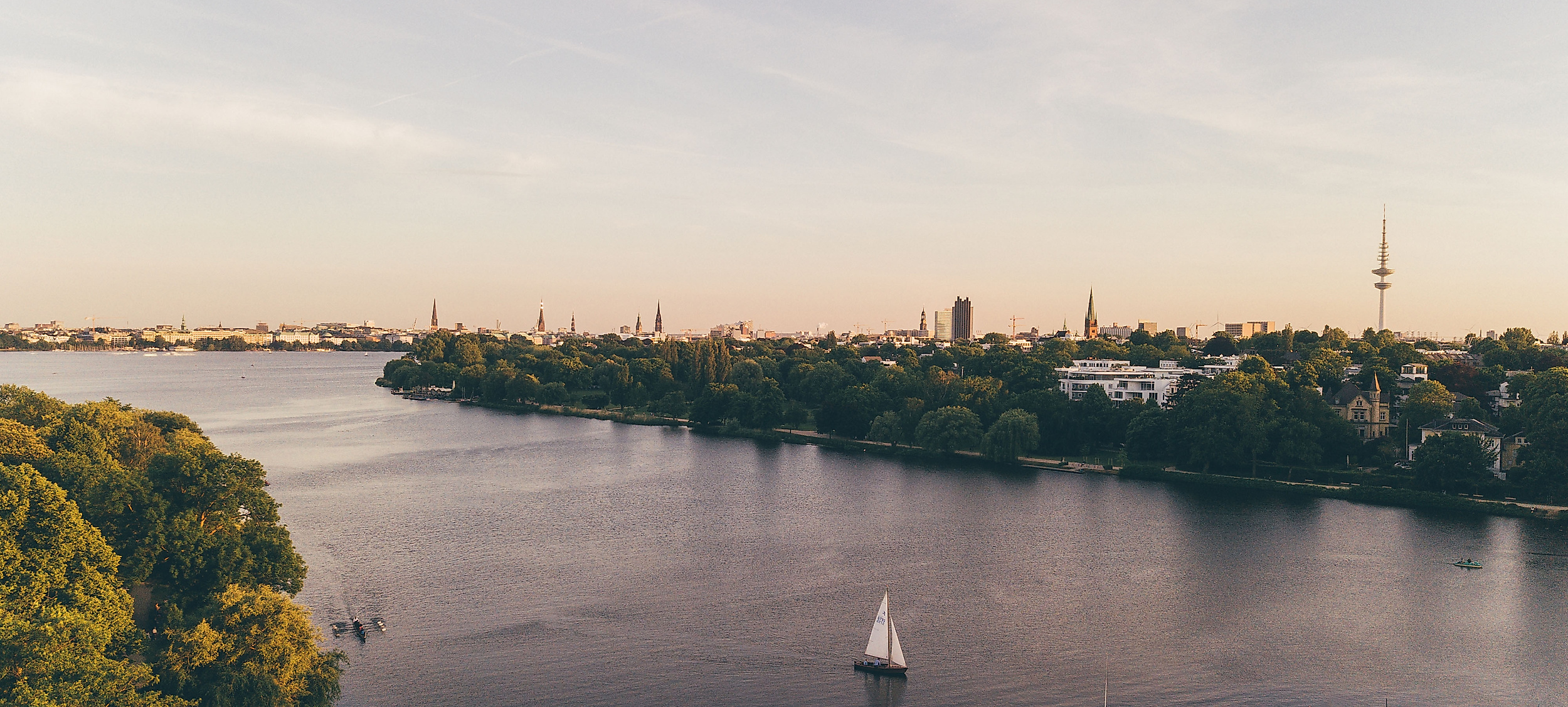 anoramablick über die Außenalster in Hamburg mit Segelbooten, grünen Ufern und Skyline im Abendlicht