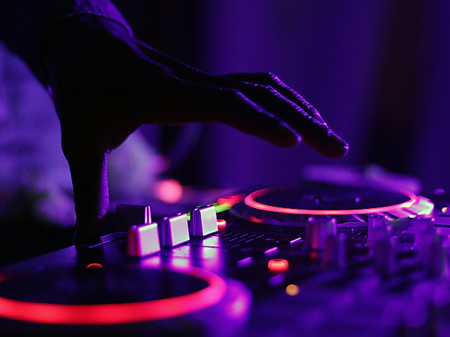DJ steuert mit Hand ein beleuchtetes Mischpult im Club, violette Lichtstimmung im Hamburger Nachtleben